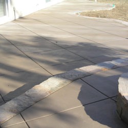 A patio with a stone bench and concrete path.