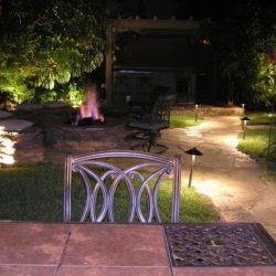 A patio with a fire pit and lights on the ground.