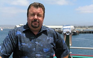 A man in a blue shirt standing on the deck of a boat.