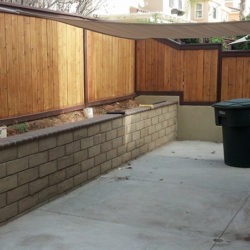 A large patio with a wooden fence and a garbage can.