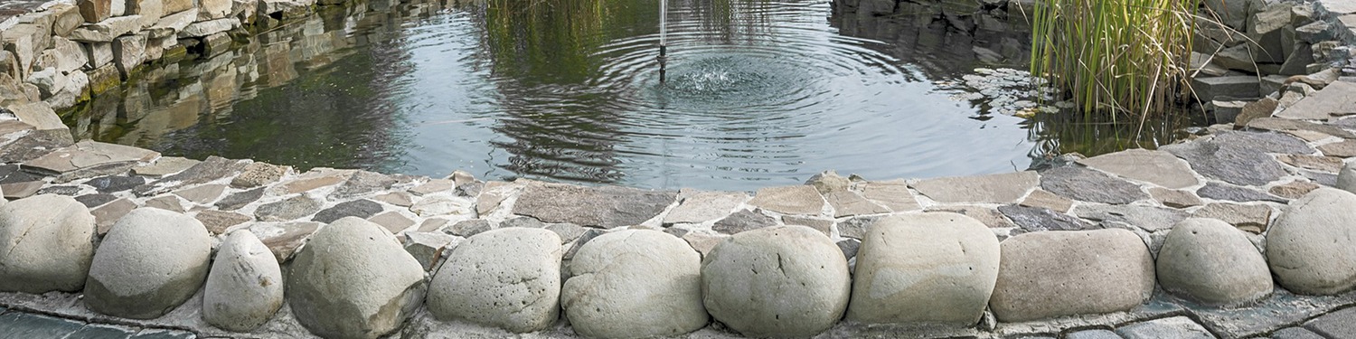 A pond with water coming out of it and rocks on the ground.